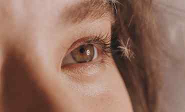 a girl's hazelnut colored eye with a dandelion near its lashes