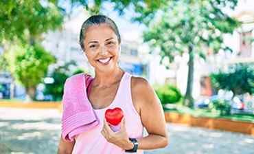 a mature woman smiling with wide teeth while holding a toy heart next to her chest